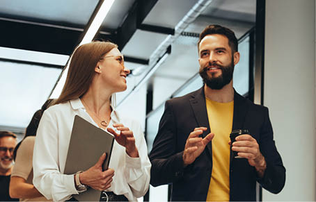 Young professionals having a discussion in a modern office. Two happy young businesspeople smiling while walking together in a hallway. Cheerful colleagues collaborating on a new project.