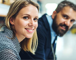 A portrait of a mature industrial man and young woman engineer in a factory, looking at camera.