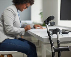 Disabled employee working in office. Orthopedic elbow crutches leaning on desk, with happy disabled African American woman working on computer in background. Working with disability concept