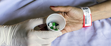 Main du soignant déposant un verre avec des médicaments dans la main patient - MACSF