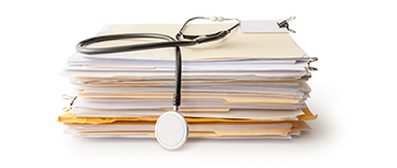 Un stéthoscope posé sur une pile de dossiers médicaux - MACSF