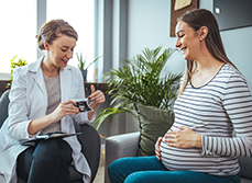 Une jeune femme sourit en regardant l'échographie que lui montre la sage-femme - MACSF