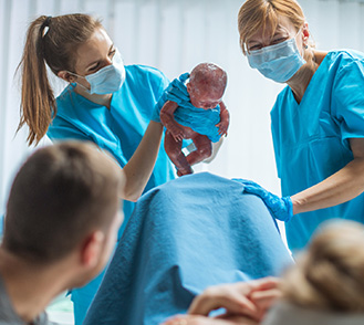 2 sages-femmes présentent un bébé à la parturiente - MACSF