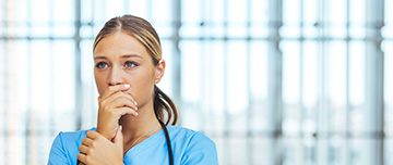 Buste d'une jeune professionnelle de santé en blouse bleue, stéthoscope autour du cou , main sur la bouche et visage angoissé - MACSF