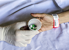 Main du soignant déposant un verre avec des médicaments dans la main patient - MACSF