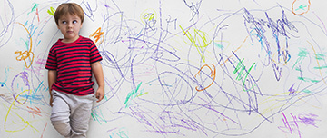 Un enfant, adossé au mur sur lequel il vient de dessiner, regarde son parent d'un air désolé - MACSF