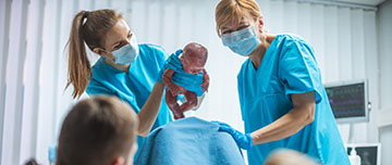 2 sages-femmes présentent un bébé à la parturiente - MACSF