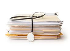 Un stéthoscope posé sur une pile de dossiers médicaux - MACSF