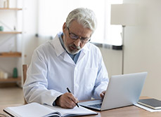 Un médecin à son bureau écrivant sur un cahier - MACSF