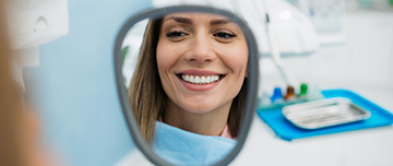 Une jeune femme souriante devant le miroir chez le dentiste - MACSF