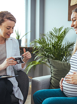Une jeune femme sourit en regardant l'échographie que lui montre la sage-femme - MACSF