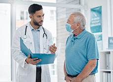 Un médecin discute avec un patient âgé et tient un dossier dans sa main - MACSF