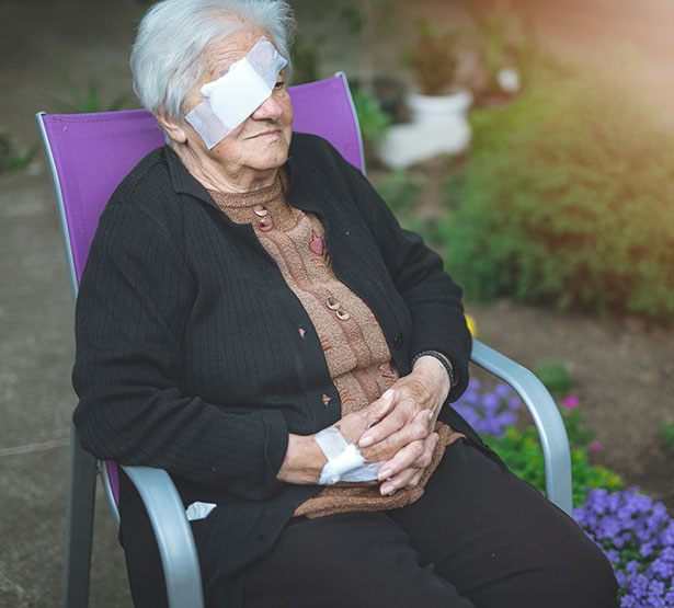 Une dame âgée portant un cache oeil est assise dans le jardin - MACSF