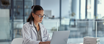 Une femme médecin à son bureau regarde l'écran de son ordinateur - MACSF