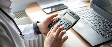 Un médecin tape sur une calculatrice devant son ordinateur - MACSF