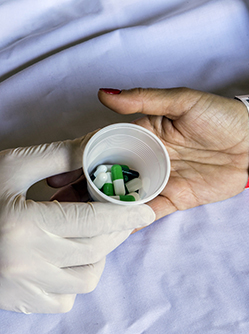 Main du soignant déposant un verre avec des médicaments dans la main patient - MACSF