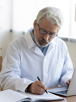 Un médecin à son bureau écrivant sur un cahier - MACSF