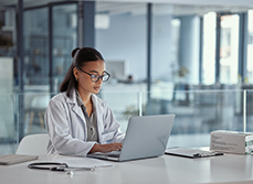Une femme médecin à son bureau regarde l'écran de son ordinateur - MACSF