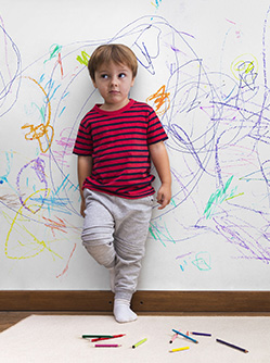 Un enfant, adossé au mur sur lequel il vient de dessiner, regarde son parent d'un air désolé - MACSF