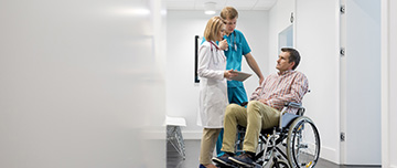 Un homme en fauteuil roulant discute avec l'infirmière dans le couloir de l'hôpital - MACSF