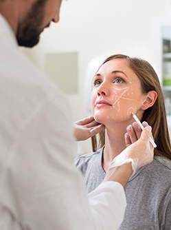 Un chirurgien fait des marques sur le visage d'une patiente en vue d'une chirurgie esthétique - MACSF