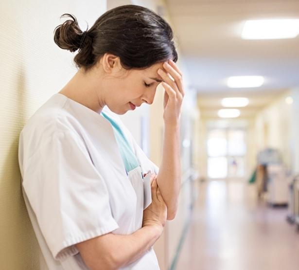 Une infirmière dépitée adossée dans un couloir d'hôpital - MACSF