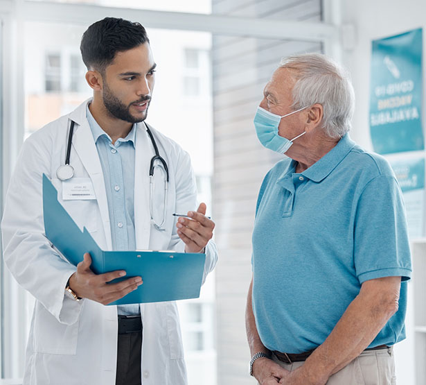 Un médecin discute avec un patient âgé et tient un dossier dans sa main - MACSF