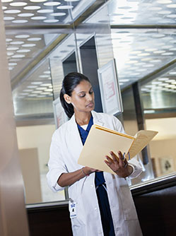 Un médecin debout dans son bureau consulte un dossier - MACSF
