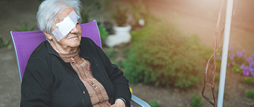 Une dame âgée portant un cache oeil est assise dans le jardin - MACSF