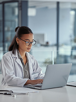 Une femme médecin à son bureau regarde l'écran de son ordinateur - MACSF