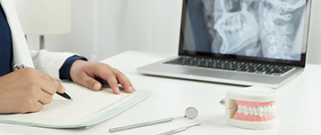 Un chirurgien-dentiste rédige un courrier face à son ordinateur - MACSF