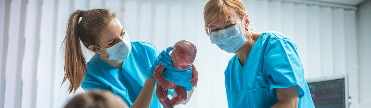 2 sages-femmes présentent un bébé à la parturiente - MACSF
