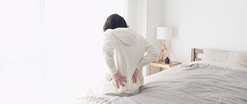 Une femme assise au bord de son lit se tenant le bas du dos - MACSF