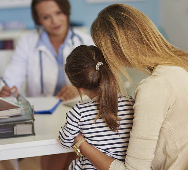 Une femme médecin à son bureau face à sa jeune patiente accompagnée de sa maman - MACSF