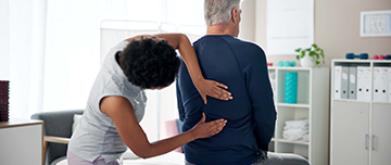 Une femme médecin examine le dos d'un patient - MACSF
