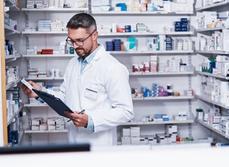 Un pharmacien consultant un cahier face au rayon de médicaments - MACSF