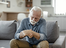 Un homme âgé, assis dans son canapé, regarde son poignet en le palpant - MACSF