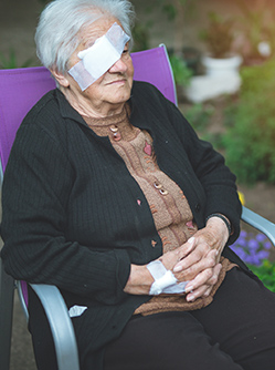 Une dame âgée portant un cache oeil est assise dans le jardin - MACSF
