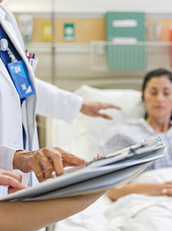 Un médecin et une infirmière regardent le dossier d'une patiente alitée - MACSF