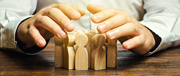 Des mains au dessus d'un groupe de personnages en bois en signe de protection - MACSF