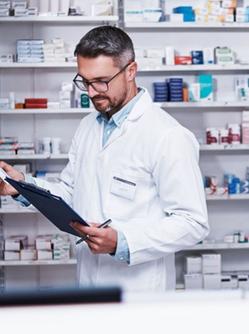 Un pharmacien consultant un cahier face au rayon de médicaments - MACSF