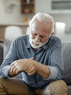 Un homme âgé, assis dans son canapé, regarde son poignet en le palpant - MACSF