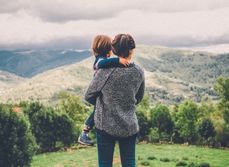 Femme de dos qui tient un enfant en regardant un paysage montagneux