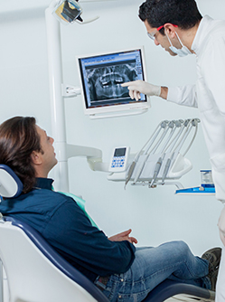 Le dentiste pointe une radio dentaire en expliquant les soins au patient - MACSF
