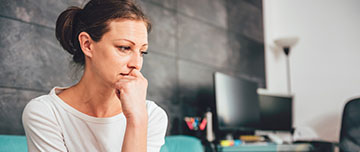 Une femme pensive assise sur son canapé - MACSF