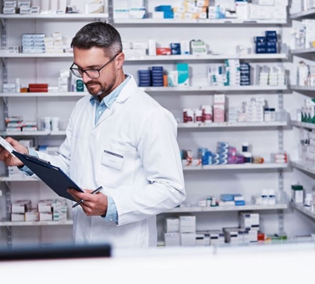 Un pharmacien consultant un cahier face au rayon de médicaments - MACSF