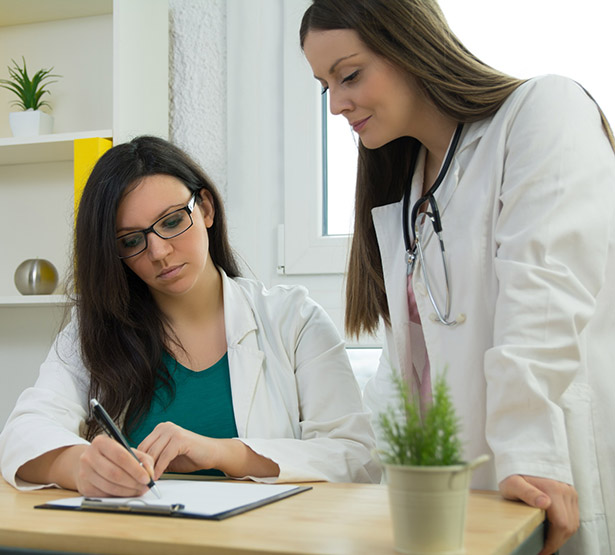 Femme médecin se tenant debout à côté de sa stagiaire assise au bureau - MACSF