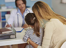 Une femme médecin à son bureau face à sa jeune patiente accompagnée de sa maman - MACSF