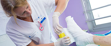 Une professionnelle de santé réalise un bandage sur le pied d'un patient - MACSF