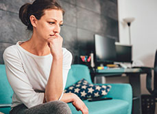 Une femme pensive assise sur son canapé - MACSF
